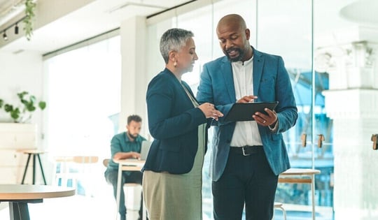Two professionals in an office reviewing data on a tablet
